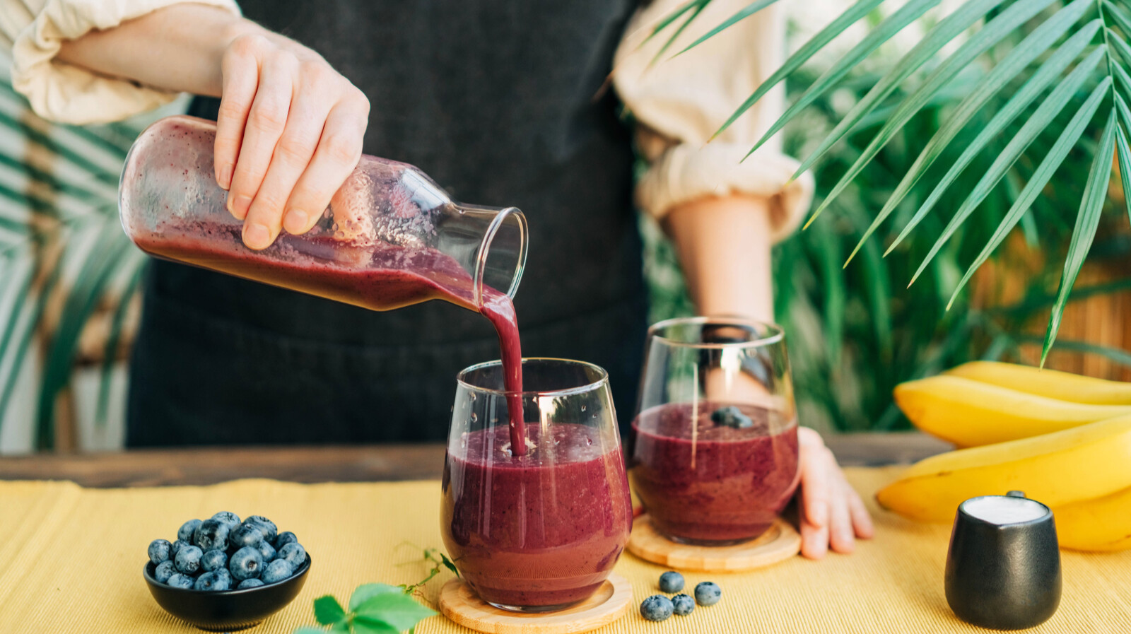 fiatal nő áfonyás smoothiet önt ki egy kancsóból két üveg pohárba
